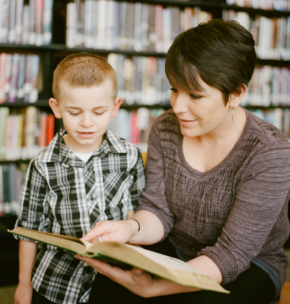 A tutor reading a book with a young boy in a library